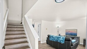 Un escalier menant à un espace de vie comprenant un canapé et un téléviseur.