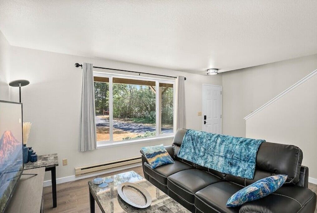 A modern living room with a leather sofa, a coffee table, and a large window offering a view of the outdoors.