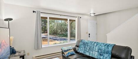 A modern living room with a leather sofa, a coffee table, and a large window offering a view of the outdoors.