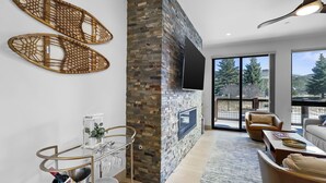 A modern living room with a stone fireplace, a mounted TV, and a glass coffee table. - Modern Townhome, Amazing views from the Rooftop Hot tub 541 (Silverthorne)