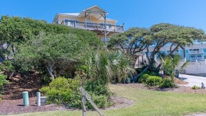 A two-story building with a balcony, surrounded by various trees and shrubs. - Ocean Views and Pool, King Bed, Beach Access at end of Driveway! (Emerald Isle)