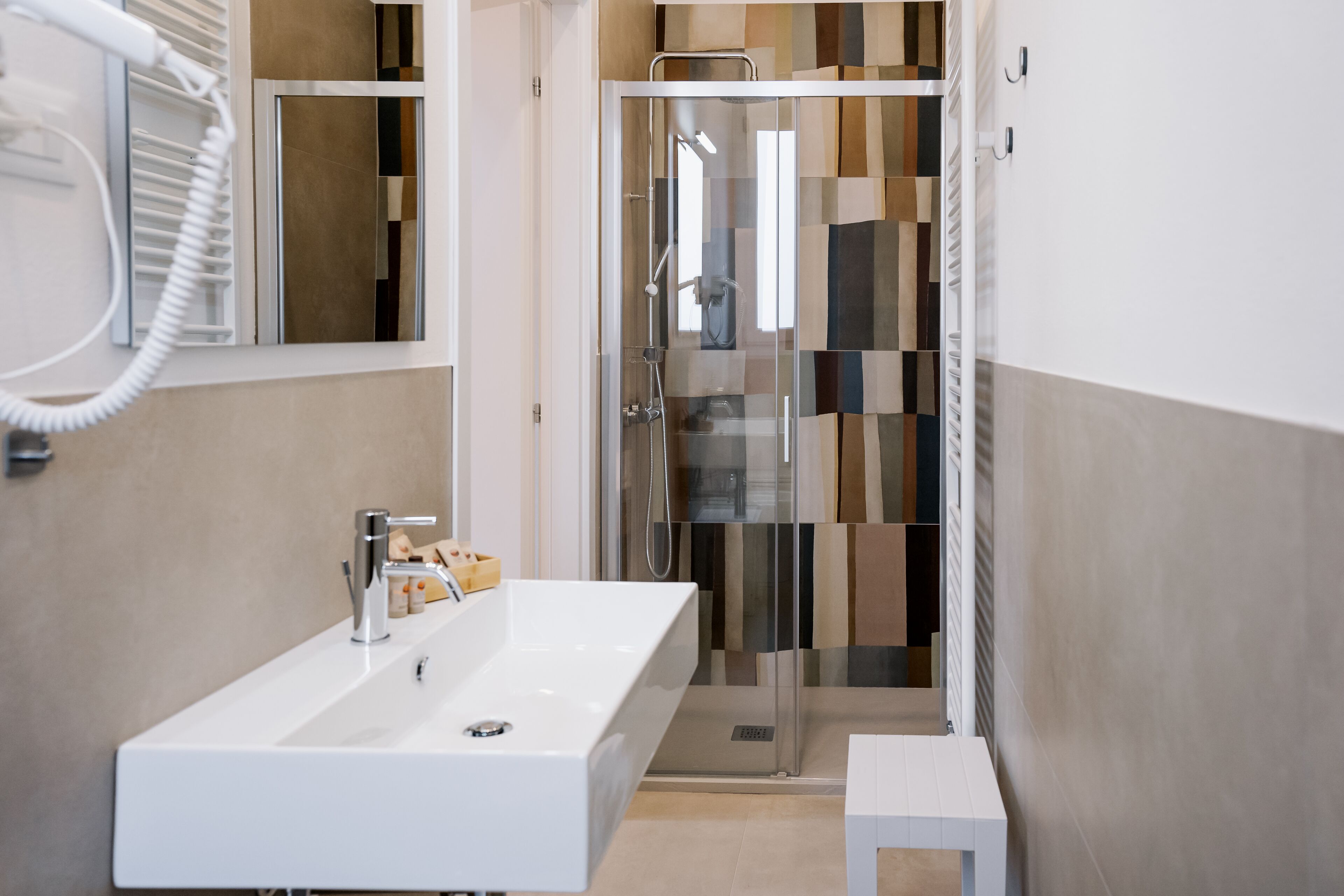 A modern bathroom with a white sink, a glass shower enclosure, and a small white stool.