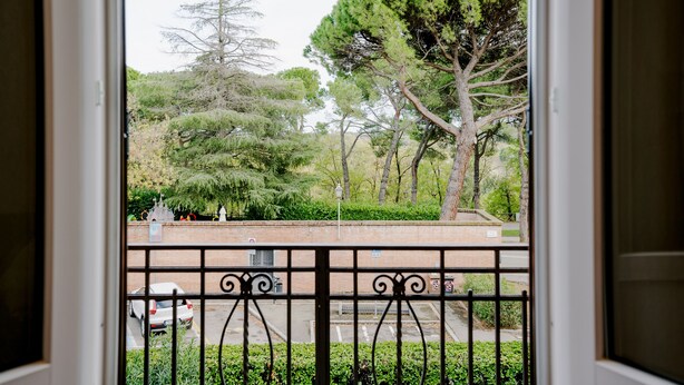 Vista de uma varanda com guarda-corpo de metal, com vista para um parque de estacionamento e um parque verde com árvores.