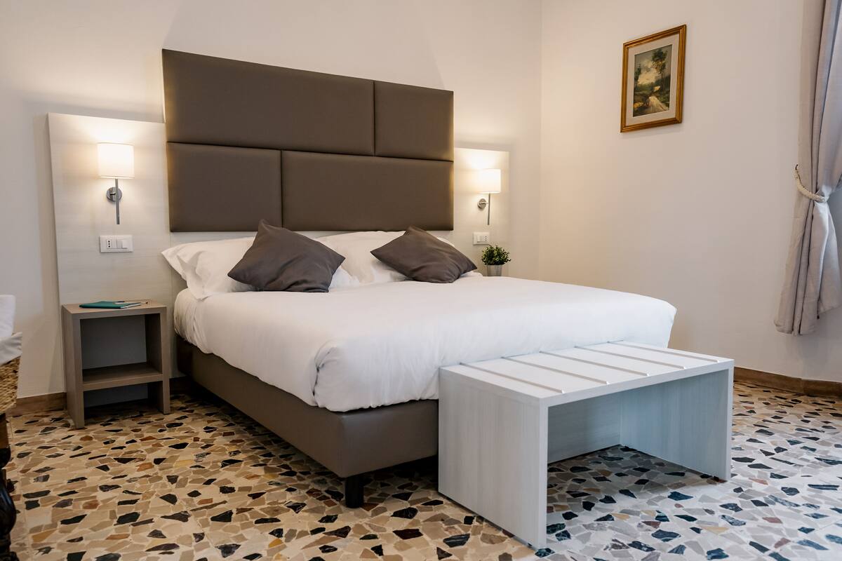 Une chambre à coucher avec un grand lit, deux tables de chevet avec des lampes, une petite plante et un sol à motifs.