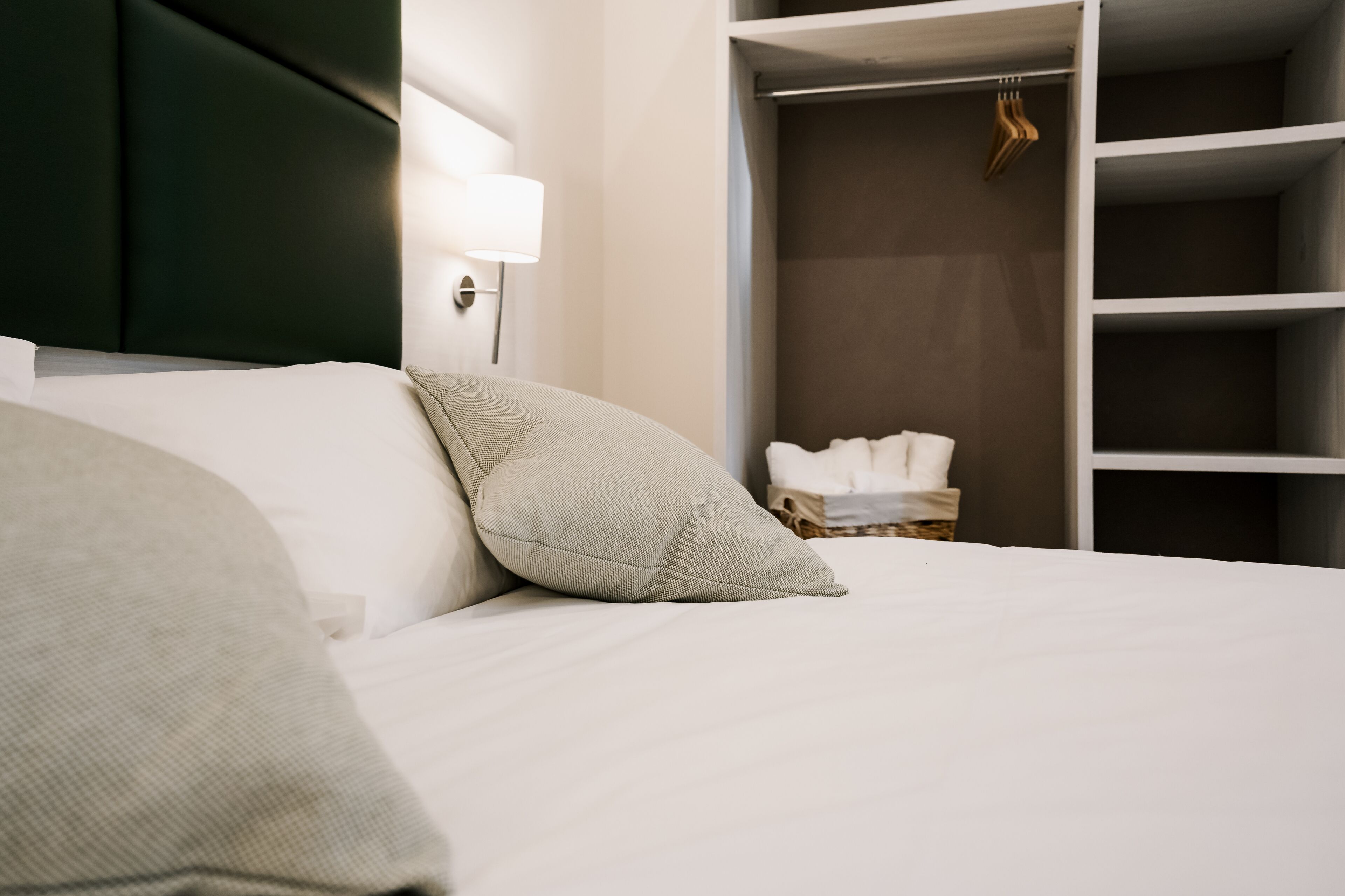 A neatly made bed with pillows, a bedside lamp, and a closet with hanging clothes.