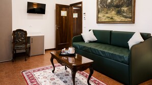 Quarto com sofá verde, uma cadeira de madeira, uma mesinha com bandeja, televisão e um quadro na parede.