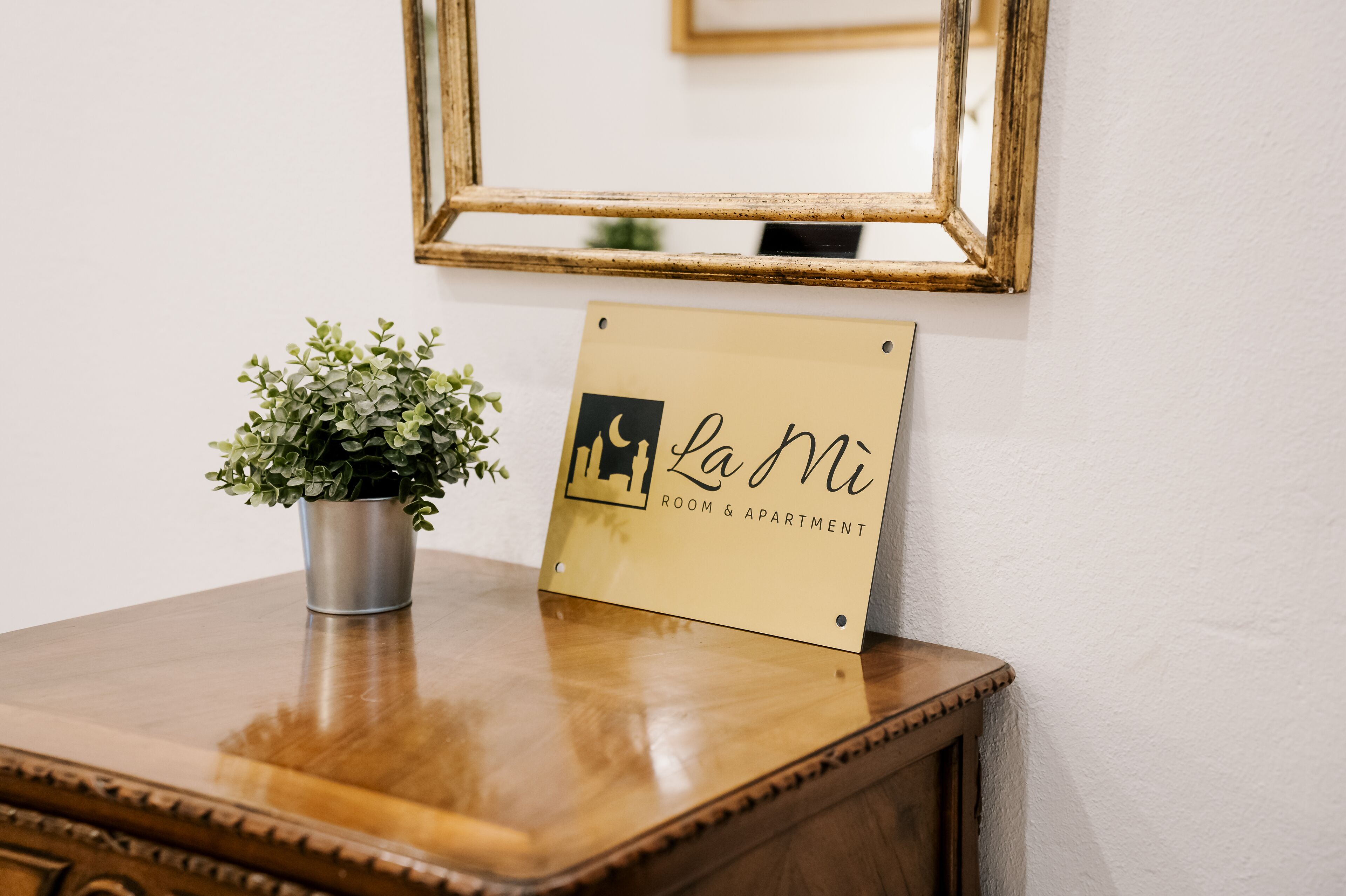 Une table en bois, sur laquelle se trouve un pot de fleurs et une pancarte indiquant « La Ni Room & Apartment ».