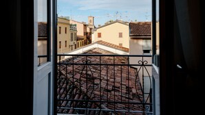 Vista pela janela com grade de metal, mostrando uma rua com edifícios e céu claro.