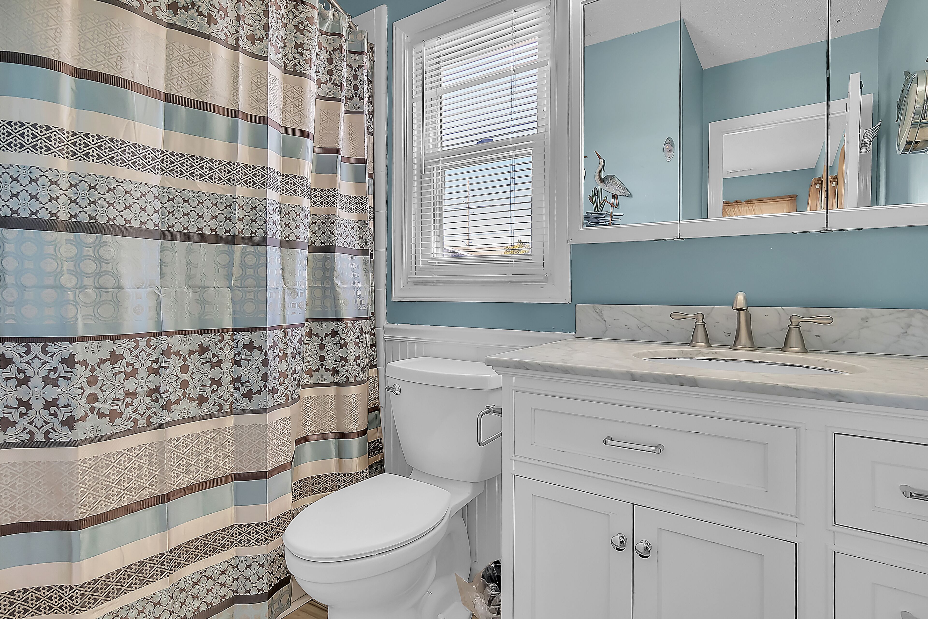 A bathroom with a striped shower curtain, a toilet, a sink with a marble countertop, and a mirror above the sink.