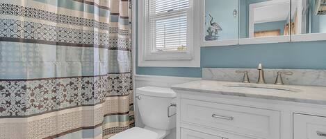 A bathroom with a striped shower curtain, a toilet, a sink with a marble countertop, and a mirror above the sink.