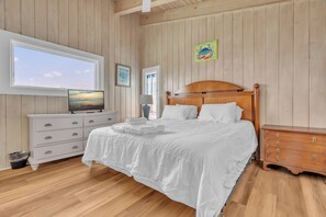 A bedroom with a wooden bed, a dresser, a television, and a window with a view of the sky. - Hot TUB & Pet Friendly, Ocean Front, Covered Decks! (Emerald Isle)