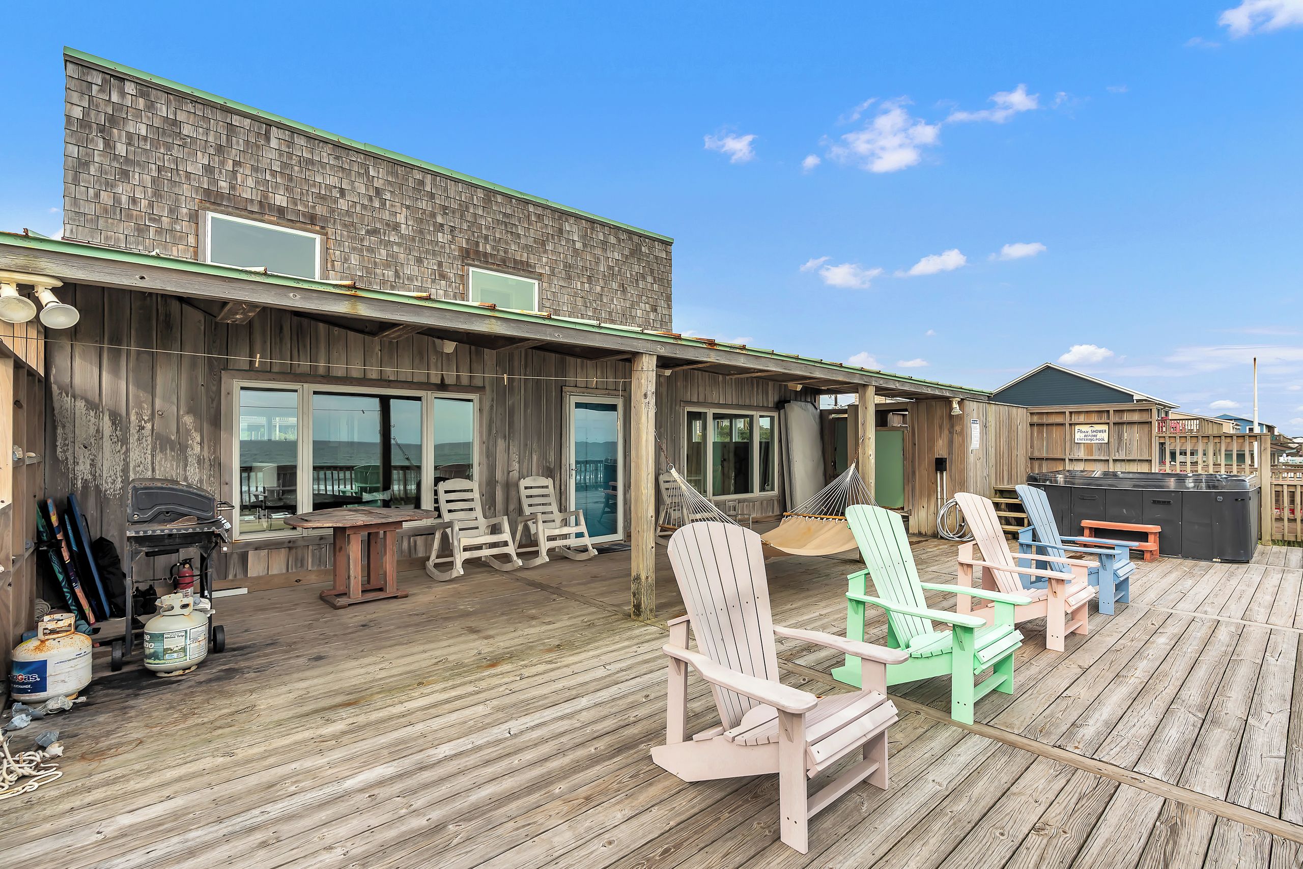 A wooden deck with Adirondack chairs, a barbecue grill, and a pool area.