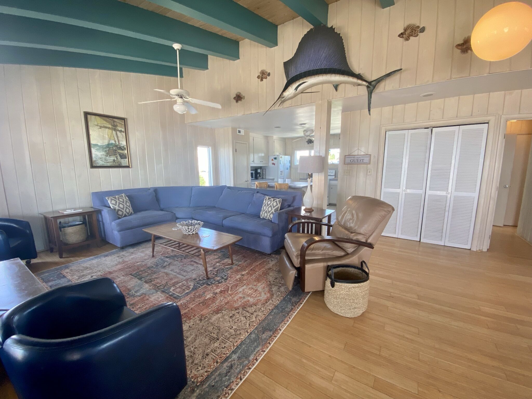 A spacious living room with a blue sectional sofa, a wooden coffee table, a leather armchair, and a patterned rug.