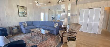 A spacious living room with a blue sectional sofa, a wooden coffee table, a leather armchair, and a patterned rug.