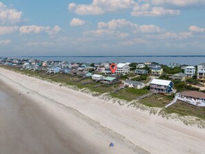 A coastal residential area with houses near the beach, a clear sky, and a calm sea in the background.
