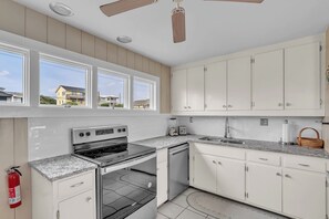 A kitchen with white cabinets, a stainless steel stove, a dishwasher, and a window overlooking a residential area.