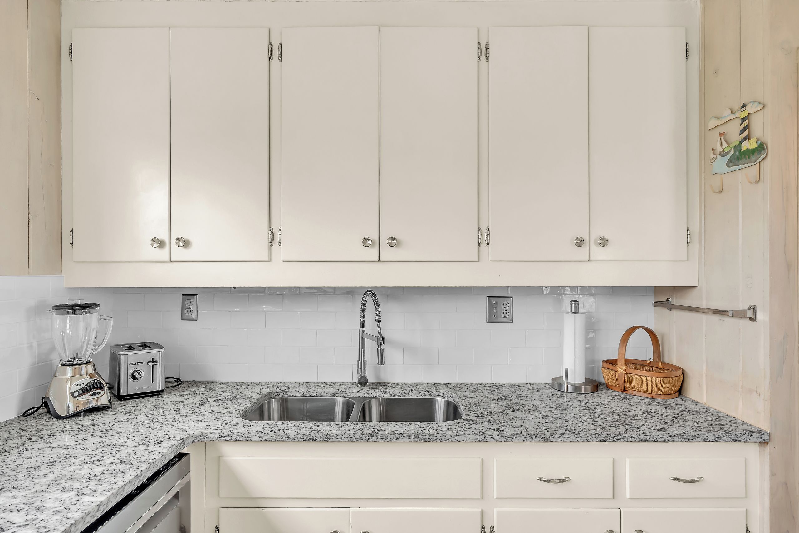 Una cocina con armarios blancos, encimera de granito, un lavabo, un tostador y una licuadora.
