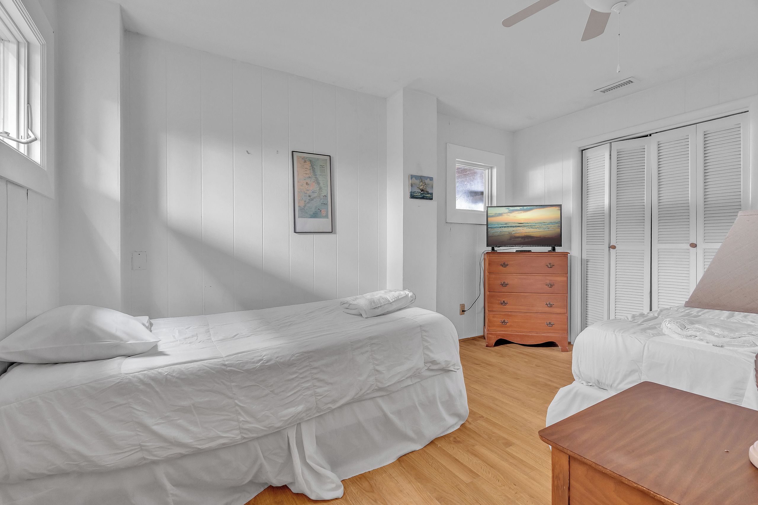 A bedroom with two beds, a dresser, a television, and a window with shutters.