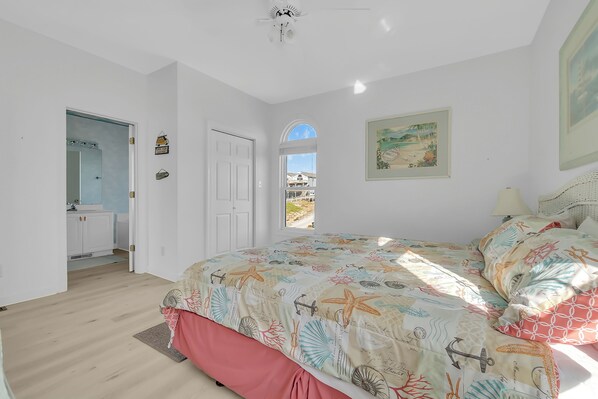A bedroom with a large bed, a window with a view, a door leading to a bathroom, and a ceiling fan. - Dogs OK! 3BR/Bonus Room - Ocean Front! (Emerald Isle)