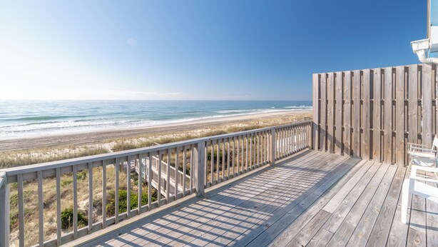 Una terraza de madera con barandilla que da a una playa.