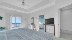 Un dormitorio con una cama grande, un aparador, un televisor y un balcón con vistas al mar.