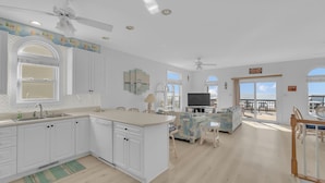 Una cocina amplia con armarios blancos, una isla central y un comedor con televisor.
