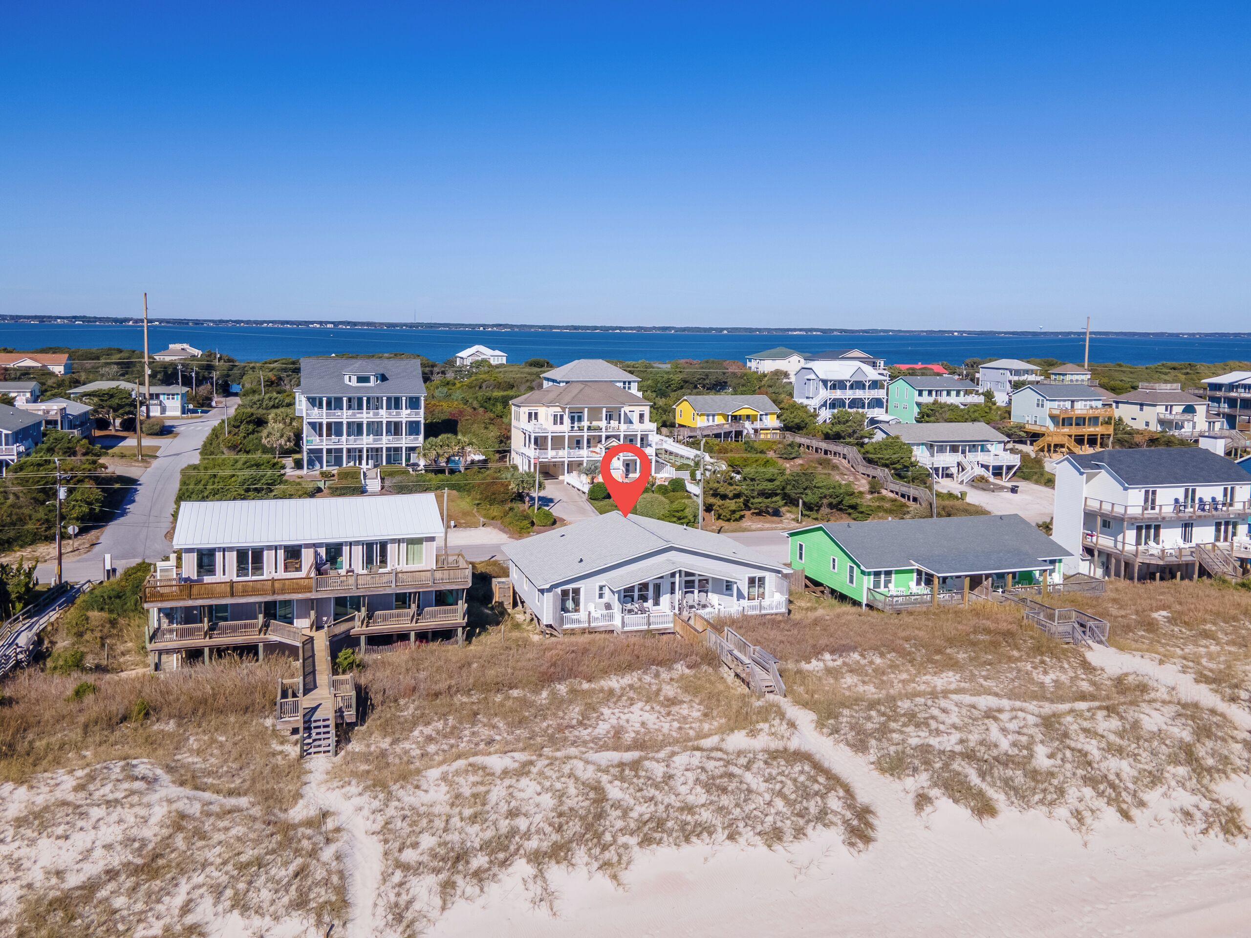 An aerial view of a coastal residential area with houses, a beach, and a clear blue sky.