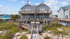 Une maison à deux étages située en bord de mer, dotée d’une terrasse en bois et de plusieurs balcons.