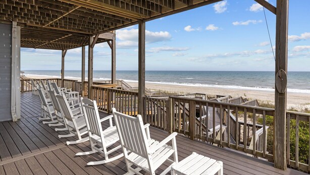 Une terrasse en bois avec des fauteuils à bascule blancs donnant sur une plage.