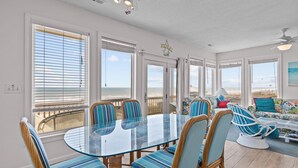 A spacious dining area with a glass table and striped chairs, large windows with blinds, and a view of the ocean. - 4BR Ocean Front Dog Friendly Duplex - Rent both sides! (Emerald Isle)