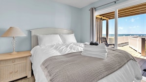 A hotel room with a bed, a nightstand, a lamp, a view of the sea, and a balcony. - 4BR Ocean Front - Dogs OK! (Emerald Isle)