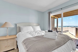 A hotel room with a bed, a nightstand, a lamp, a view of the sea, and a balcony. - 4BR Ocean Front - Dogs OK! (Emerald Isle)