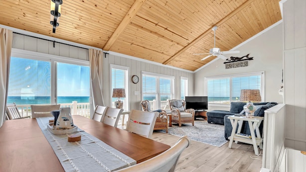 A spacious living area with a wooden ceiling, large windows, a dining table, and a TV. - 4BR Ocean Front - Dogs OK! (Emerald Isle)