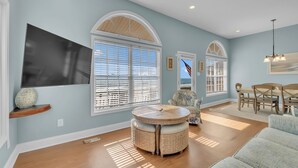 A spacious living area with a large TV, a round table, and a dining set. - 4BR Ocean Front - DOG OK - Close to town! (Emerald Isle)