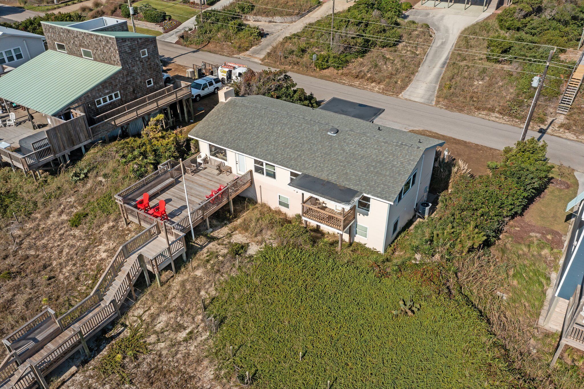 An aerial view of a house with a large deck, a covered porch, and a road nearby.