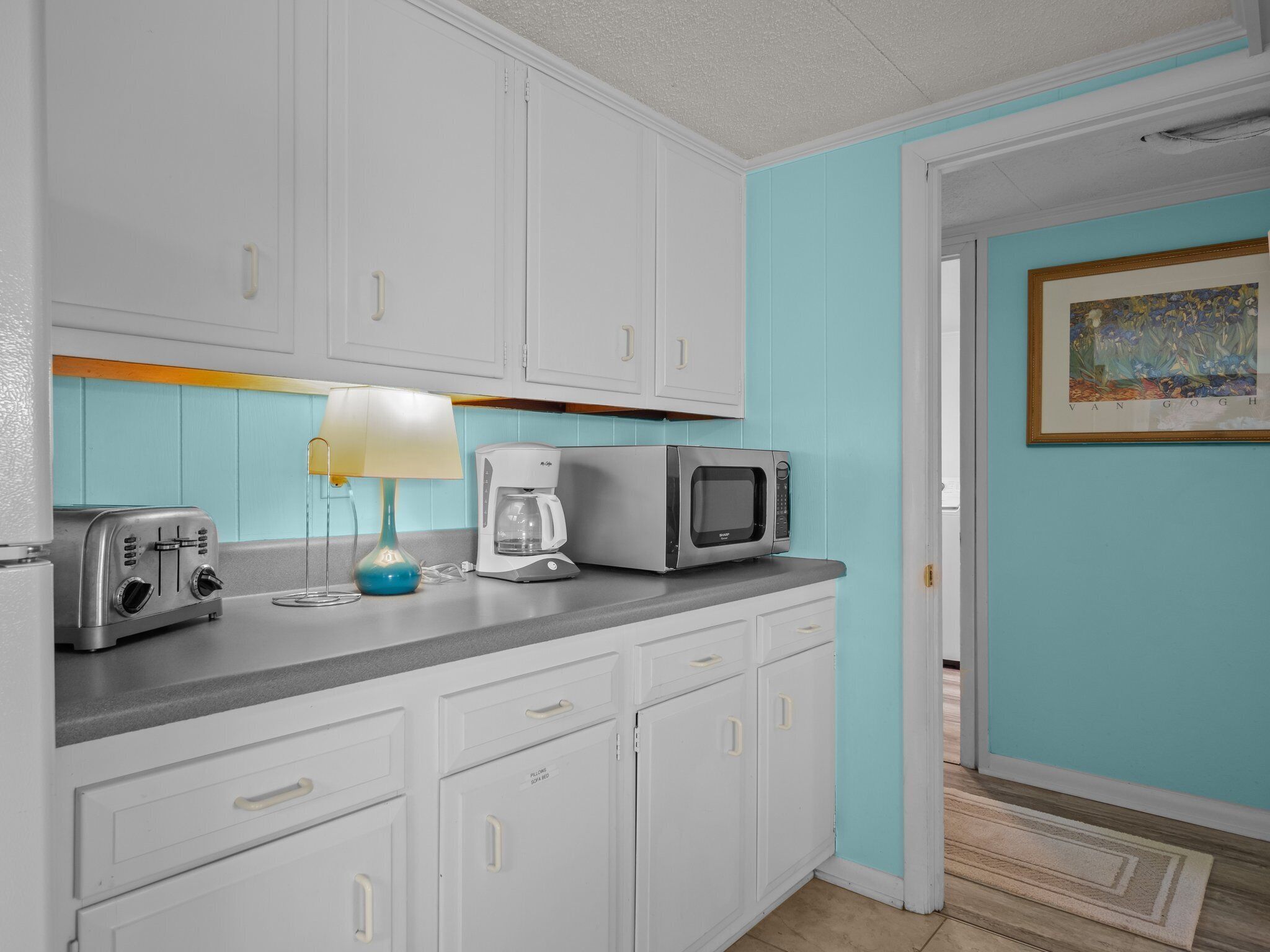 A compact kitchen with white cabinets, a toaster, a coffee maker, and a microwave.