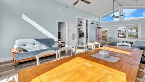 A spacious living area with a wooden dining table, a blue sofa, and a ceiling fan. - 3BR - One Level - SUPER CUTE - Ocean front & DOGS OK!! (Emerald Isle)