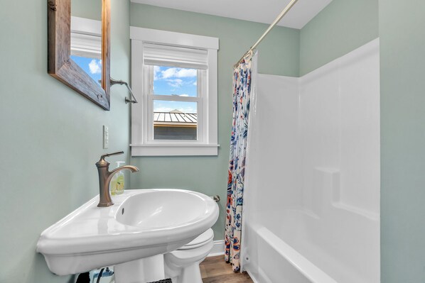 A bathroom with a white sink, toilet, and bathtub. There is a window above the sink and a shower curtain with a floral pattern. - 3BR - One Level - SUPER CUTE - Ocean front & DOGS OK!! (Emerald Isle)