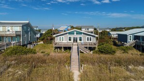 A beachfront property with a central house, a wooden deck, and a sandy path leading to the house. - 3BR - One Level - SUPER CUTE - Ocean front & DOGS OK!! (Emerald Isle)