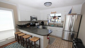 A kitchen with white cabinets, a stainless steel refrigerator, a built-in oven, and a bar area with stools. - 3BR- Dogs OK- Ocean Front - Master Suite (Emerald Isle)