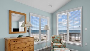 A room with a wooden dresser, a chair, a floor lamp, and large windows with blinds.