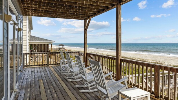A wooden deck with white rocking chairs overlooking a beach.