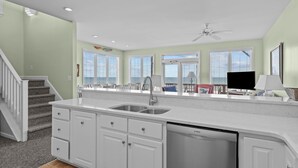 A kitchen with white cabinets, a dishwasher, and a large window overlooking the ocean.
