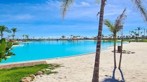 Ein großer, klarer Pool, umgeben von Palmen und einem Sandstrand.