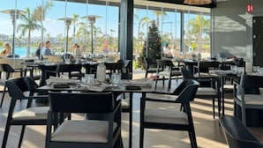 Ein modernes Restaurant mit hohen Decken, gewebten Pendelleuchten und großen Fenstern mit Blick auf den Pool und Palmen.