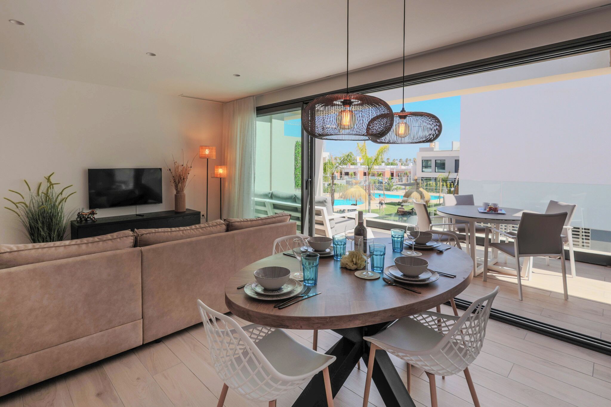 A modern dining area with a round table set for four, a sofa, and a TV on a stand.