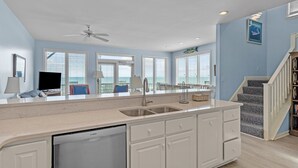A spacious kitchen with a large island, white cabinetry, and a Bosch dishwasher. There are multiple windows providing natural light, and a staircase leading to a lower level. - 4BR duplex close to town and ocean front! (Emerald Isle)