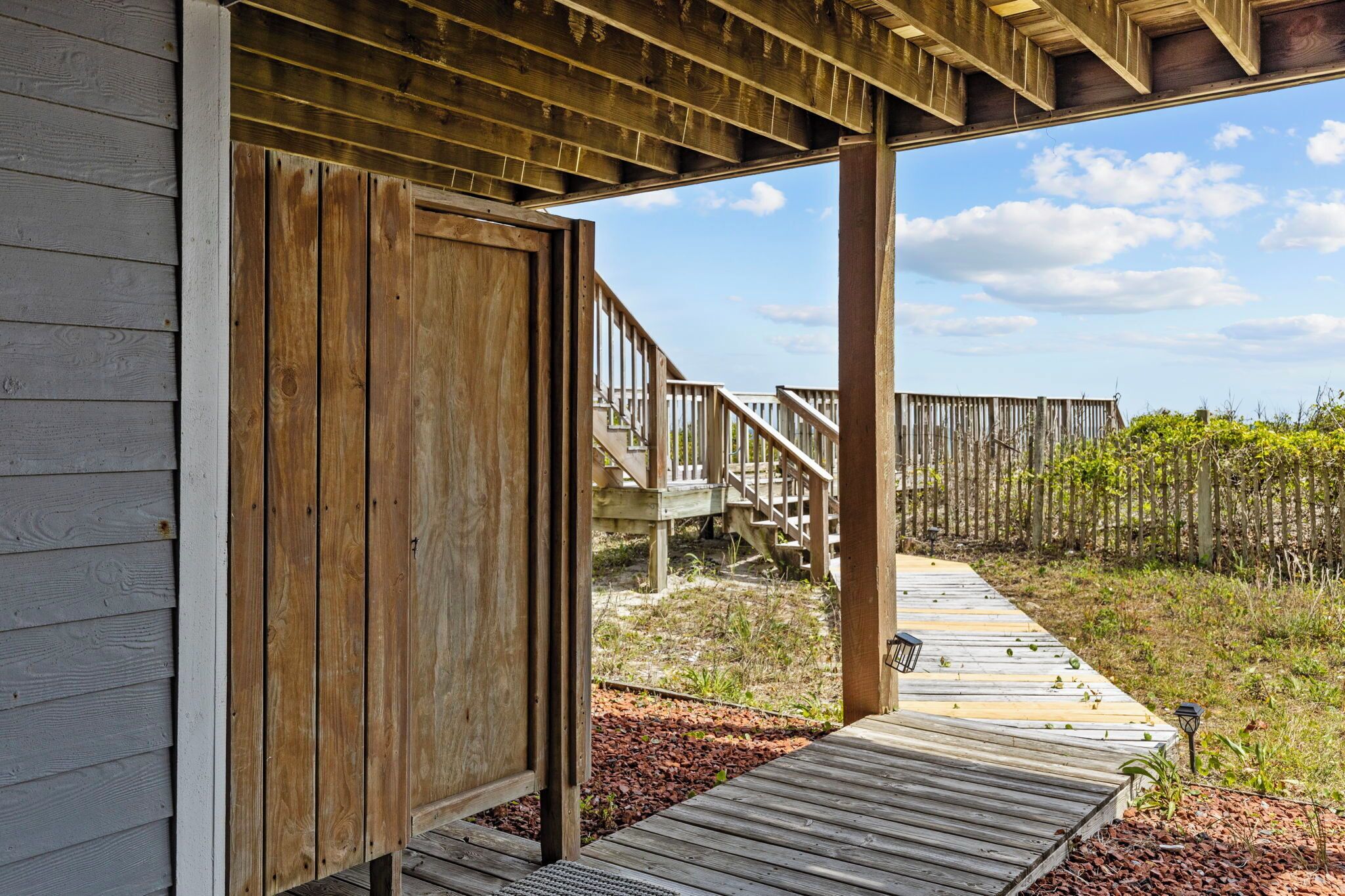 A wooden deck leading to a covered area with a wooden door, a wooden staircase, and a view of a natural landscape.