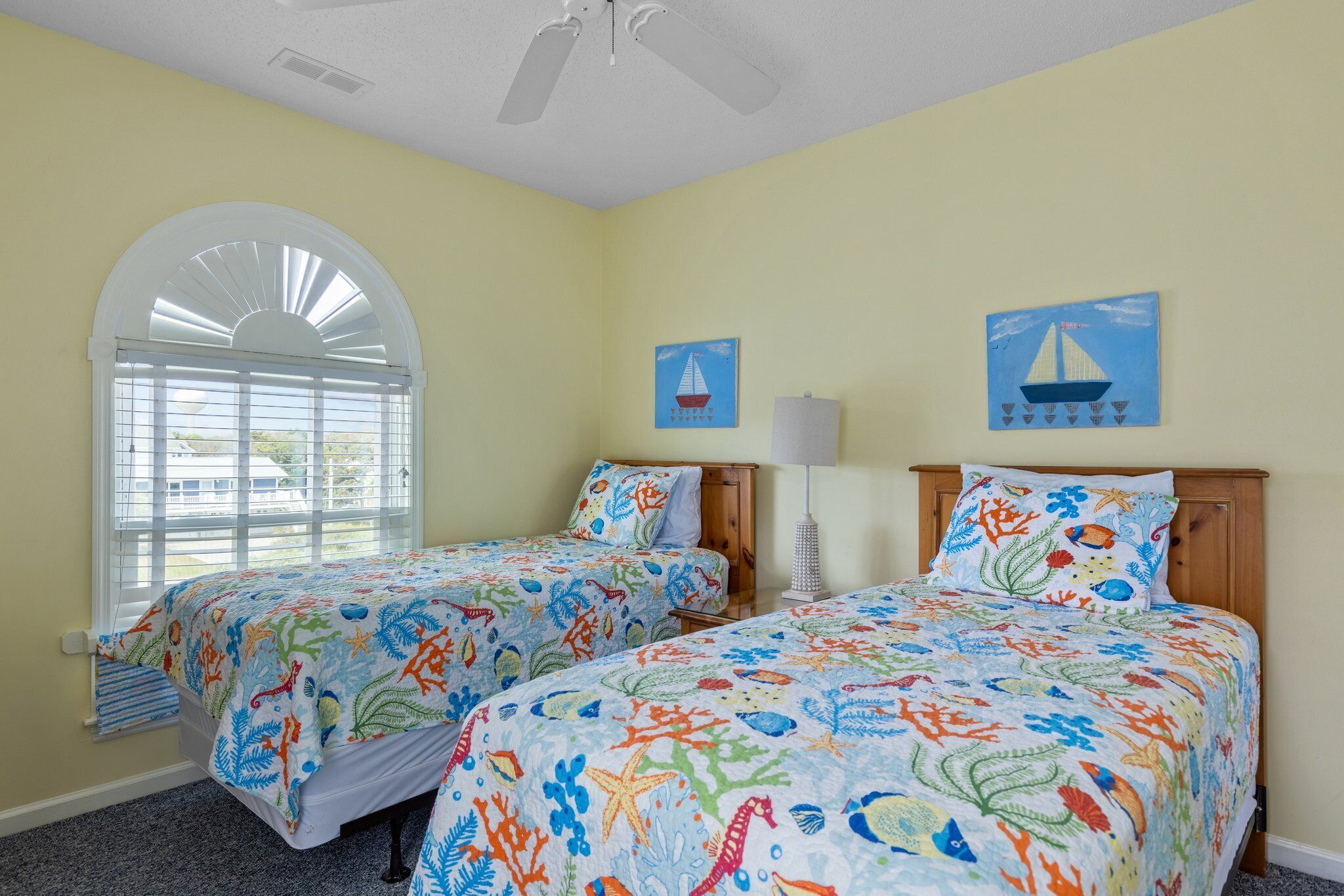 A room with two beds, a ceiling fan, and a window with blinds.
