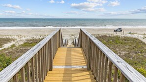 A wooden boardwalk leading to a beach with a vehicle parked on the sand. - 4BR duplex close to town and ocean front! (Emerald Isle)